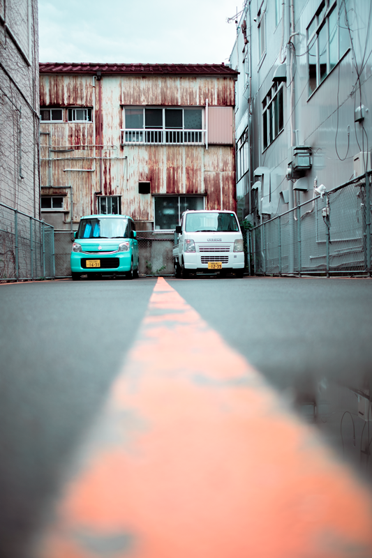 2 parked cars in an industrial looking area, in the streets of Japan